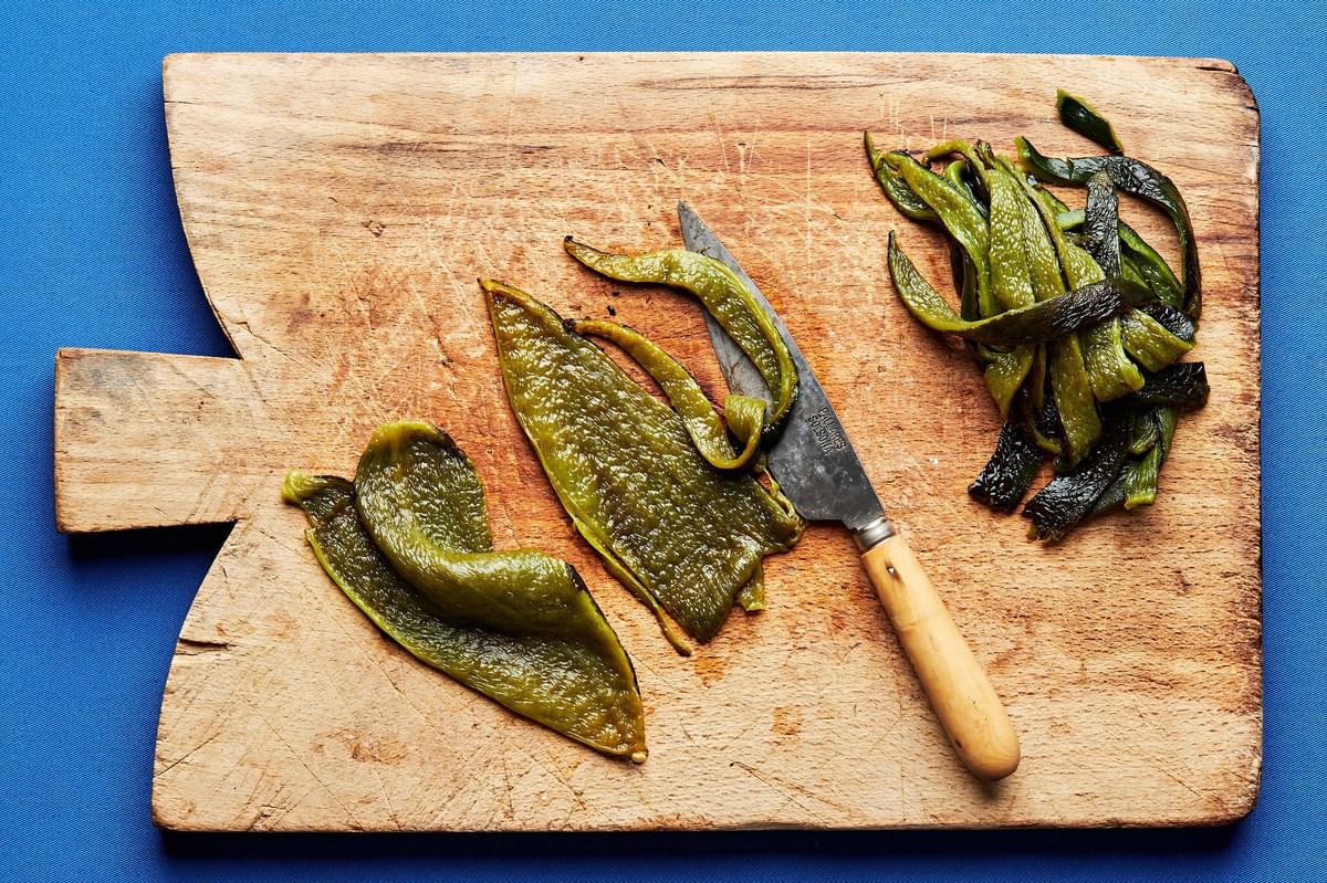 roasted poblano peppers  with the skins, cores, stems and seeds removed being sliced on a cutting board