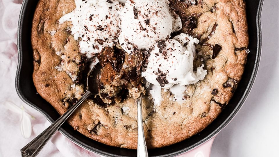 Salty Dark and Milk Chocolate Skillet Cookie with ice cream and 2 spoons with a pink linen and white flowers