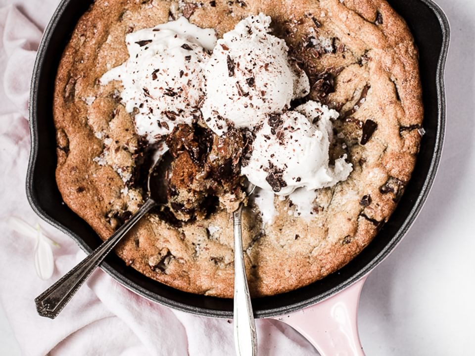 Salty Dark and Milk Chocolate Skillet Cookie with ice cream and 2 spoons with a pink linen and white flowers