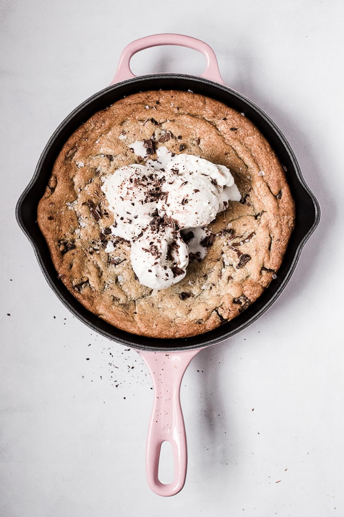 freshly baked chocolate chip skillet cookie in a pink cast iron skillet with ice cream