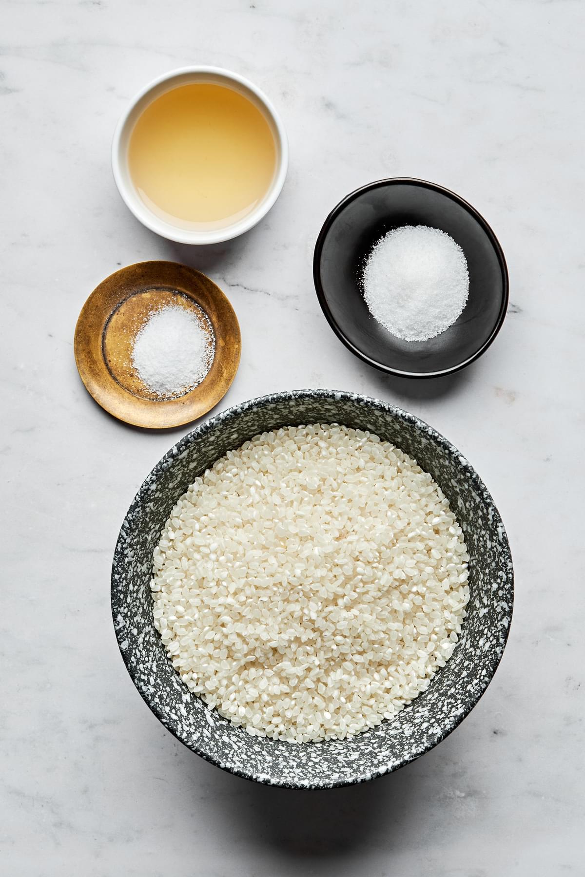 raw sushi rice, salt, unseasoned rice vinegar and sugar in bowls on the counter to make sushi rice