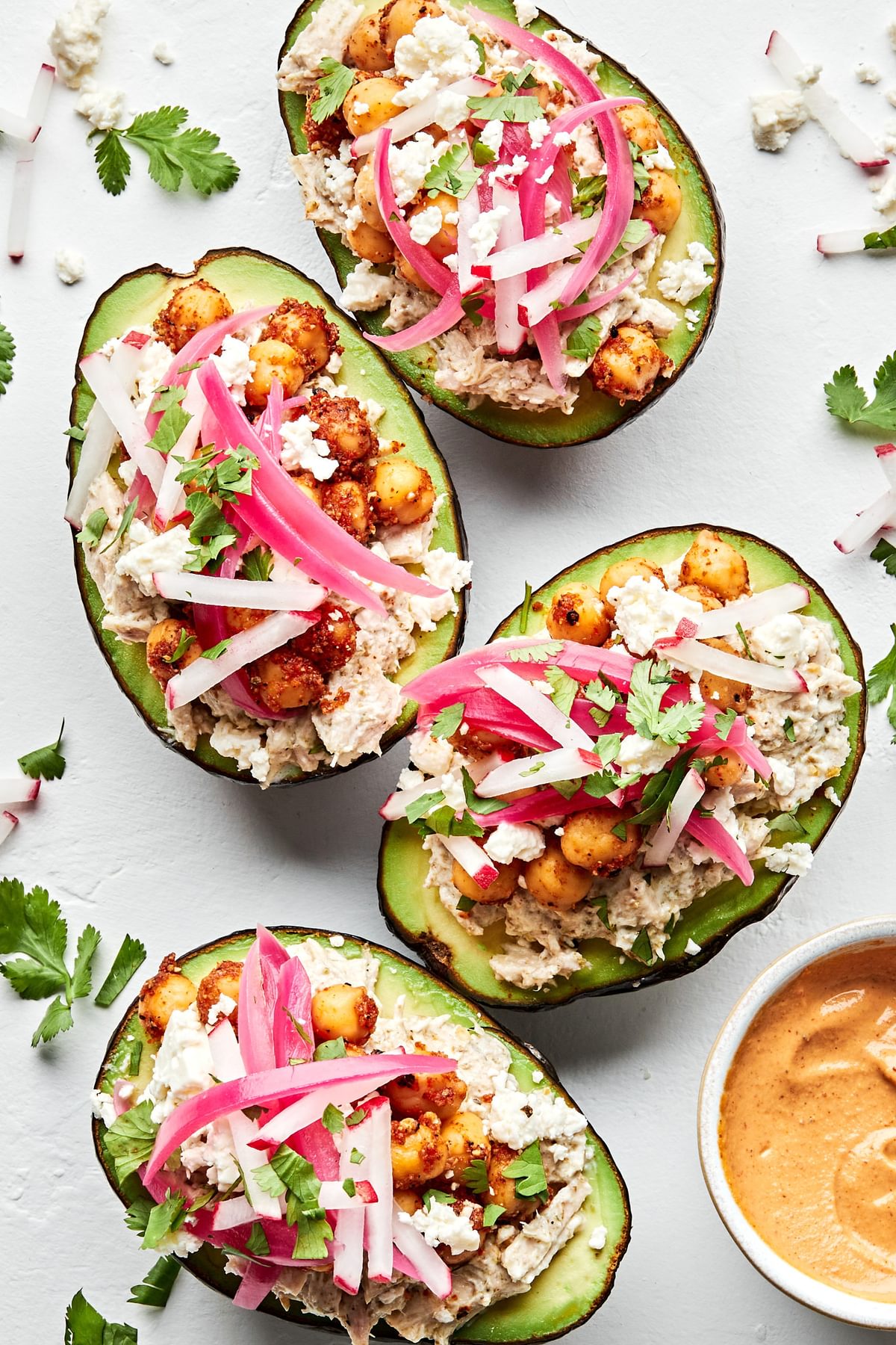 2 avocados stuffed with tuna salad, topped with pickled red onions, feta cheese and vegan cashew cheese sauce