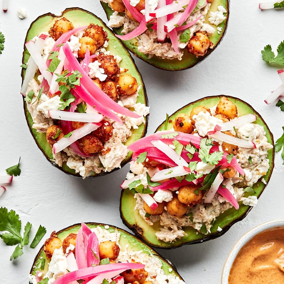2 avocados stuffed with tuna salad, topped with pickled red onions, feta cheese and vegan cashew cheese sauce