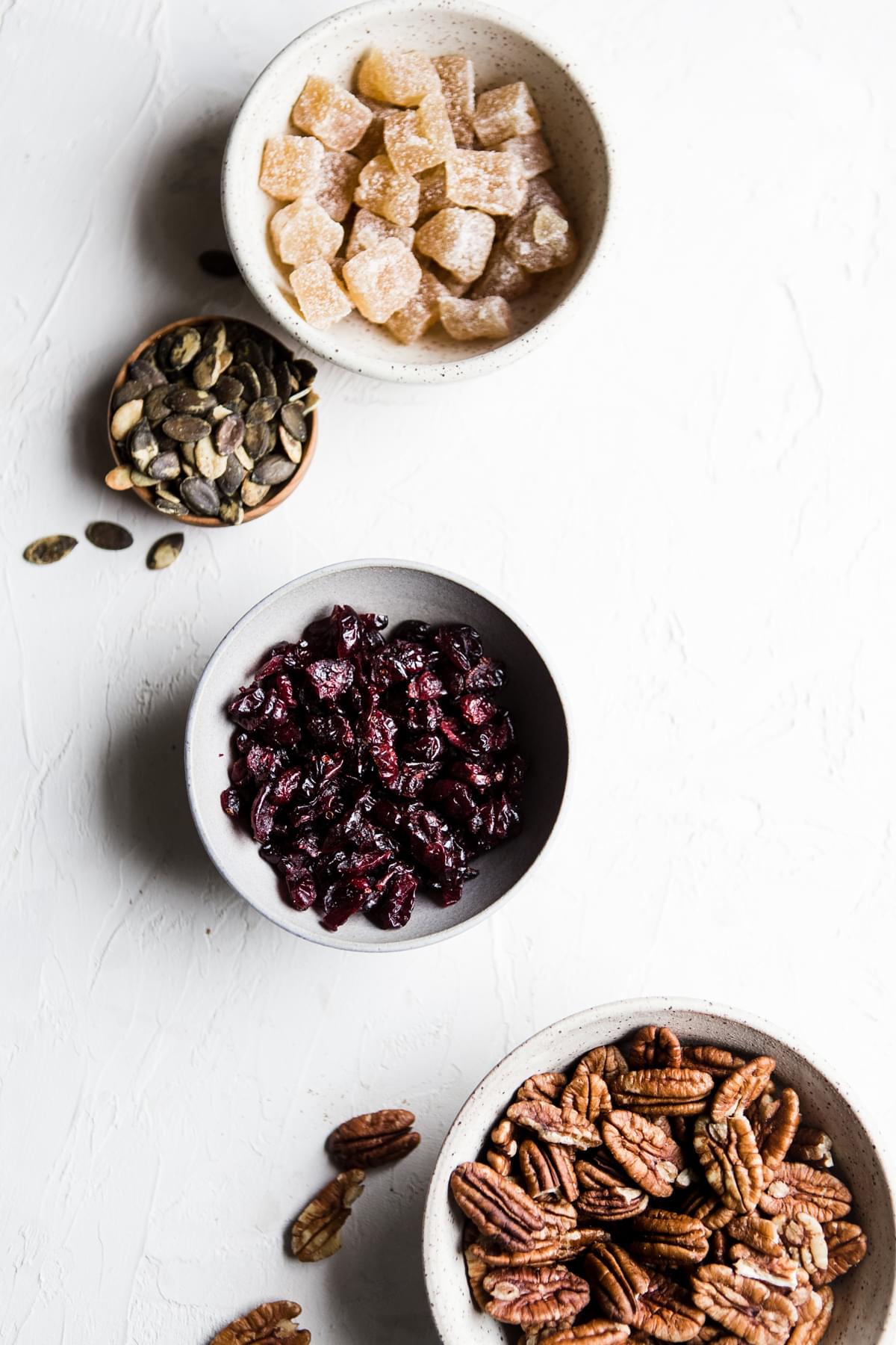 candied ginger, pumpkin seeds, dried cranberries and pecan halves in bowls