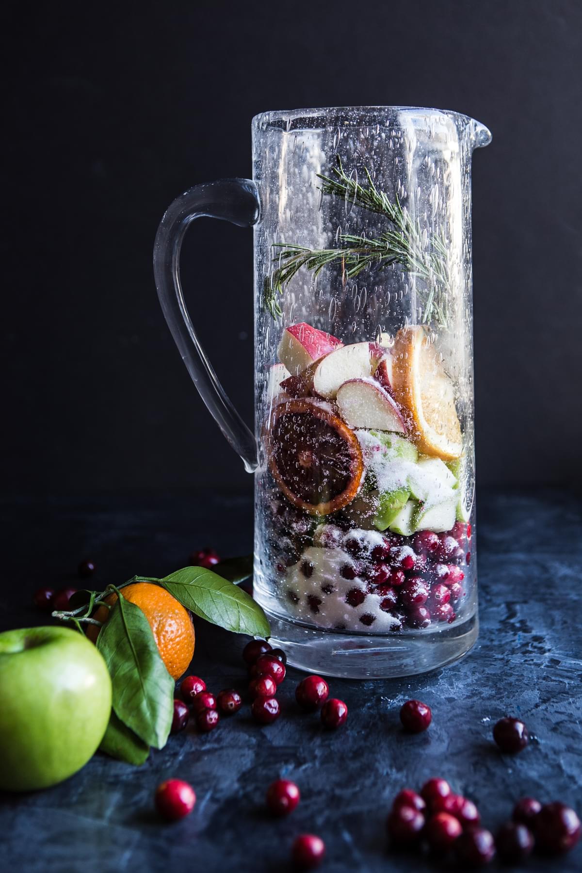 apples, oranges, cranberries and rosemary, sugar and cinnamon in a pitcher for red sangria
