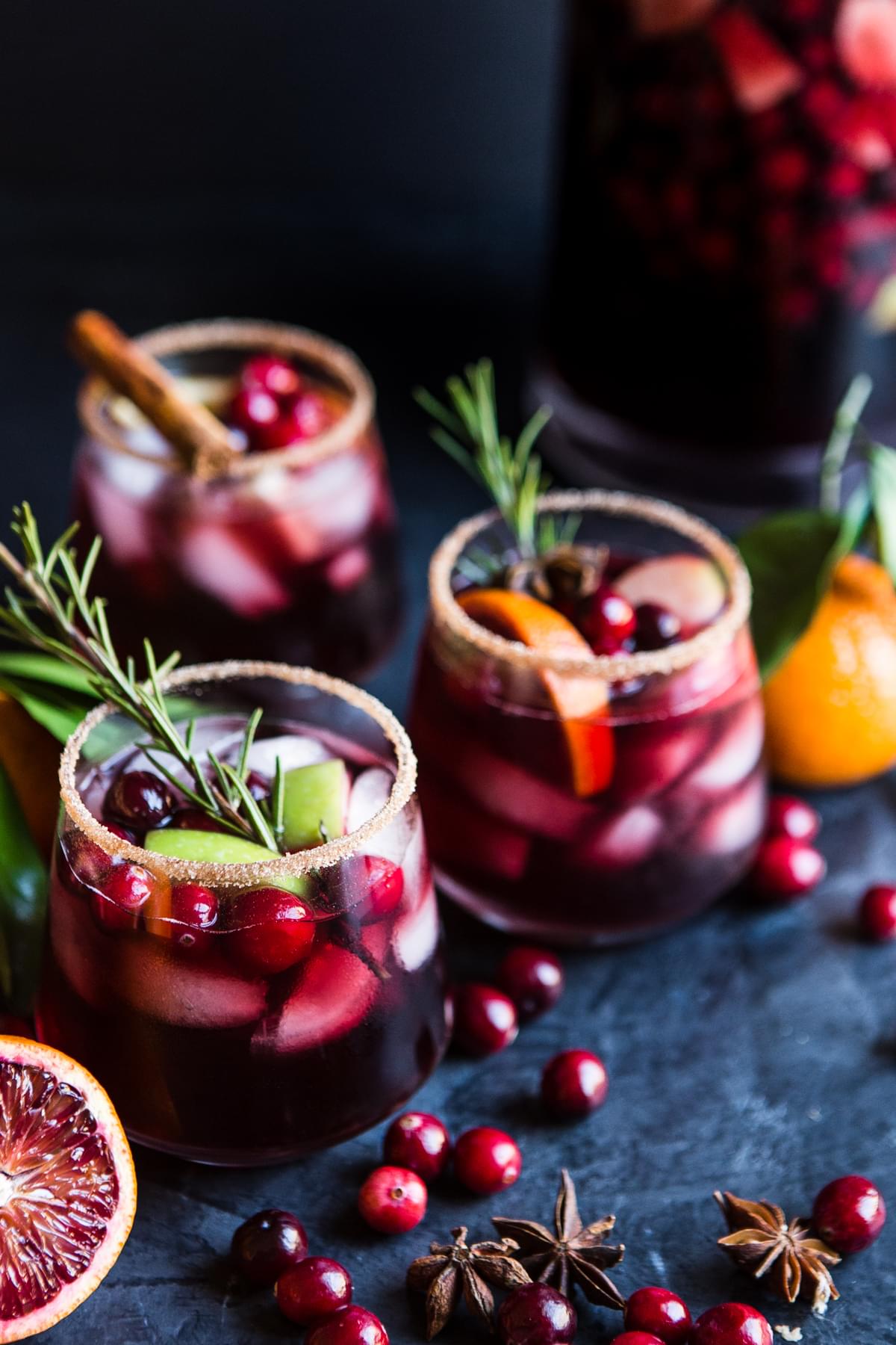 3 glasses filled with red wine sangria made with cranberries, apples, oranges, cinnamon and brandy garnished with rosemary