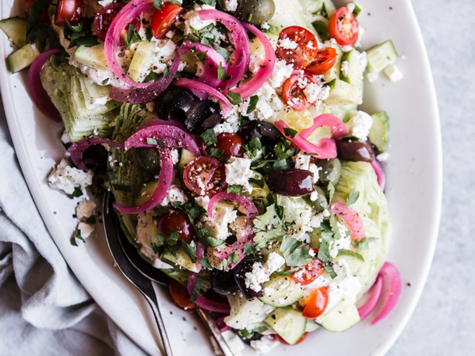 Mediterranean Wedge salad with pickled onions, olives feta dressing and cucumbers and tomatoes on a plate