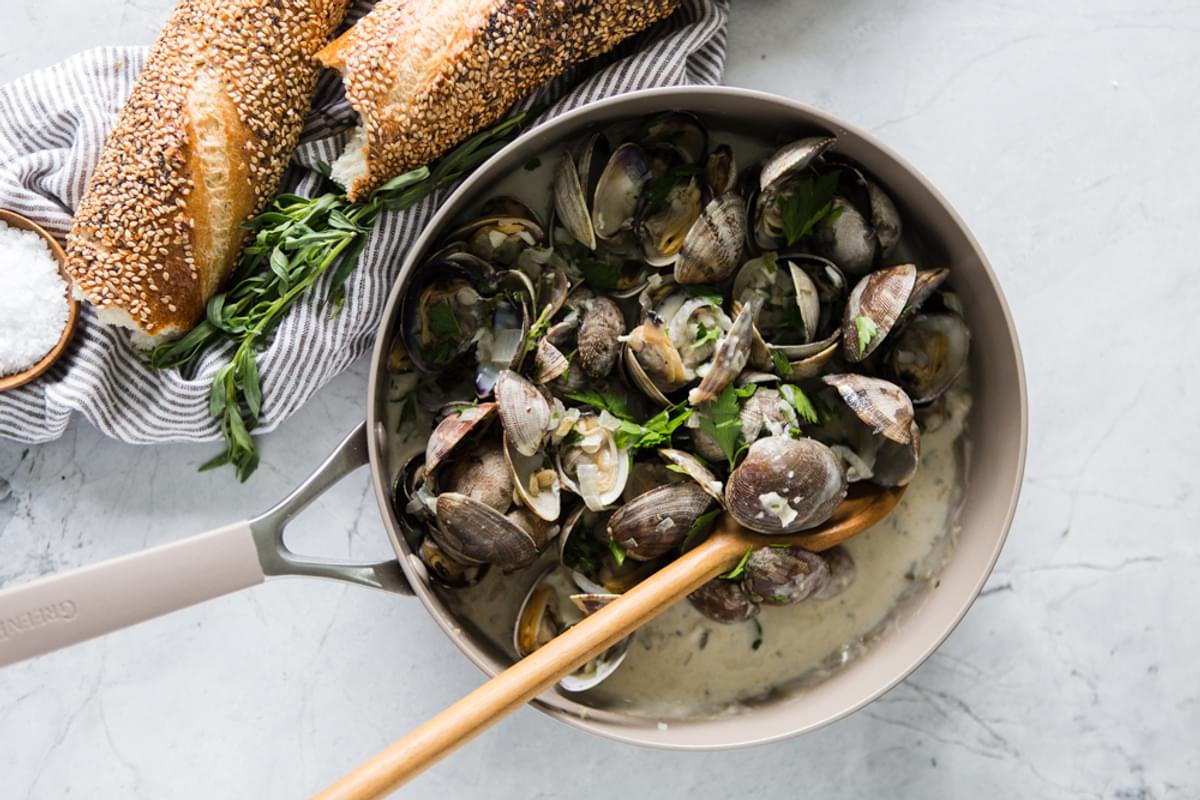 Steamed Clams With Linguini in a white wine sauce in a pan next to a baguette on a linen