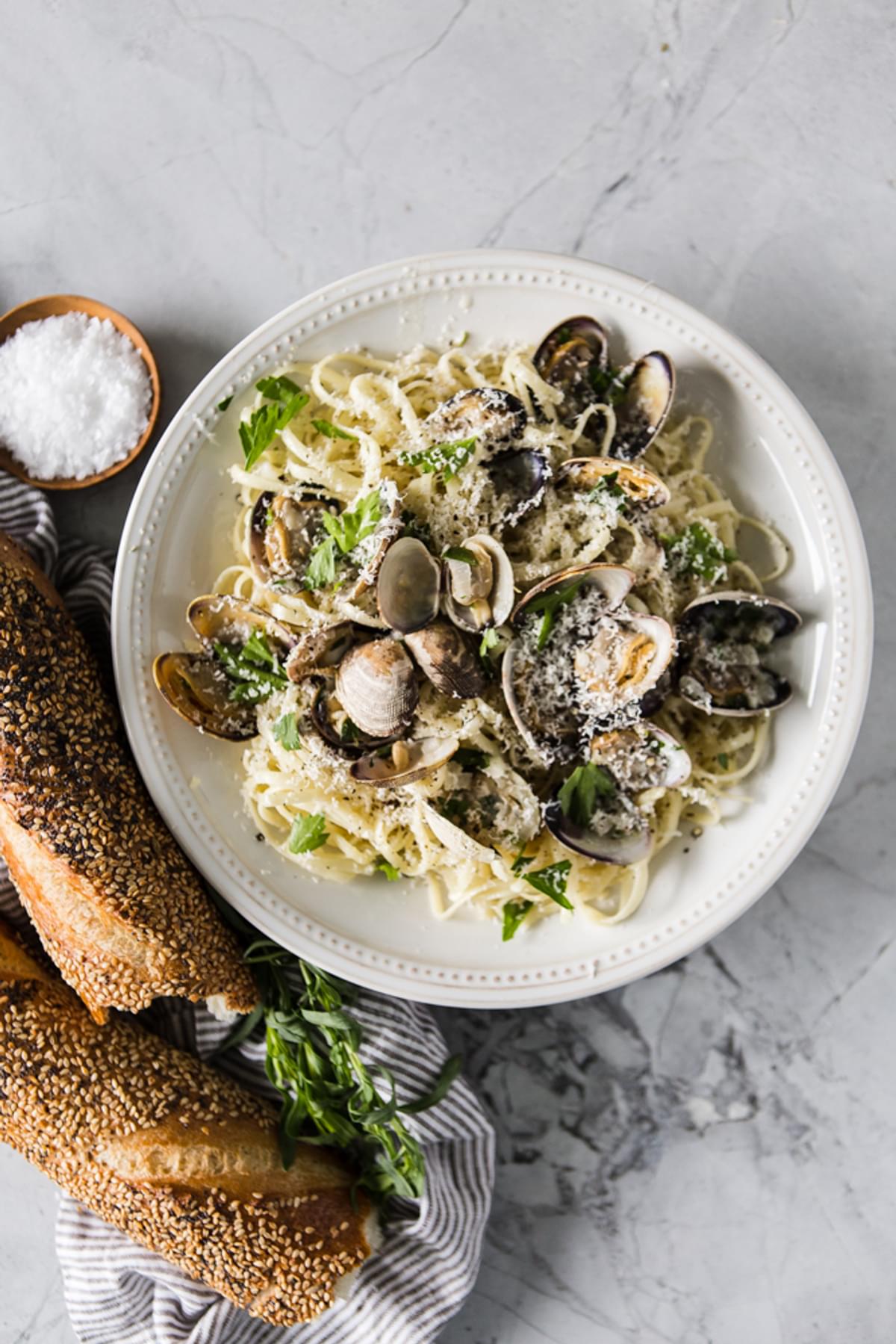 a bowl of Steamed Clams With Linguini a loaf of bread with a linen
