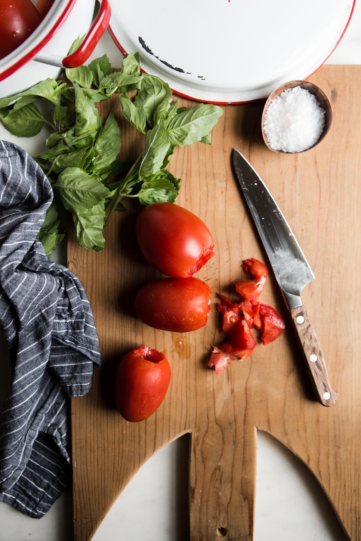 tomatoes, basil and salt on a cutting board with a knife and a linen