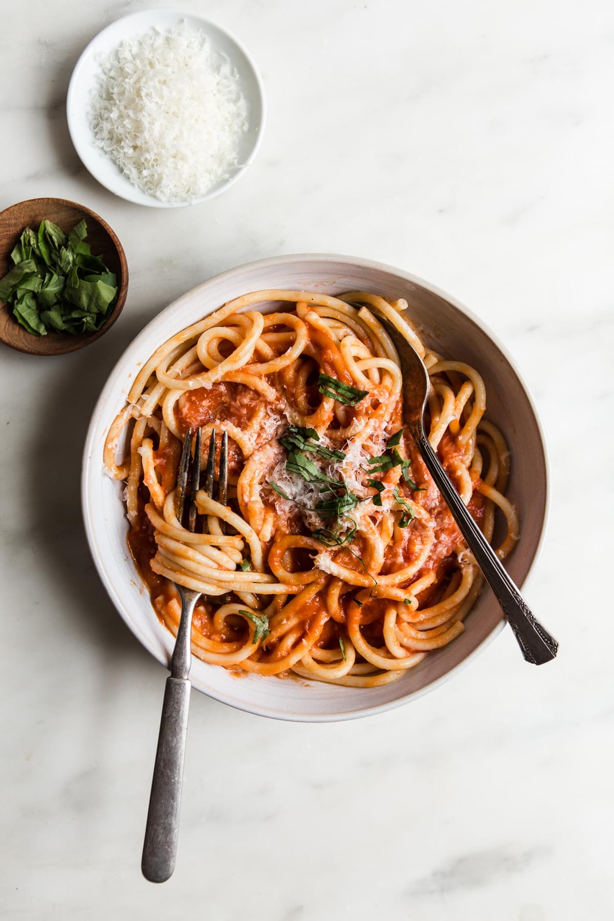 Three Ingredient pomodoro sauce with noodles in a bowl with fresh basil and parmesan cheese and two forks swirled in pasta