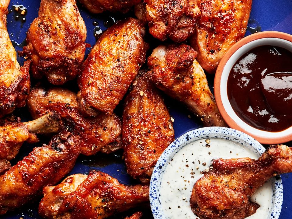 Homemade baked chicken wings on a plate served with ranch dressing and bbq sauce in small bowls