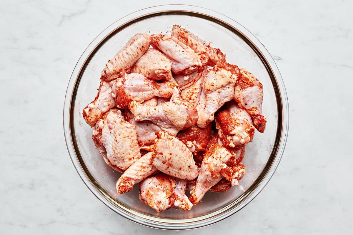 raw chicken wings in a glass bowl seasoned with salt, pepper, garlic powder, paprika and cayenne
