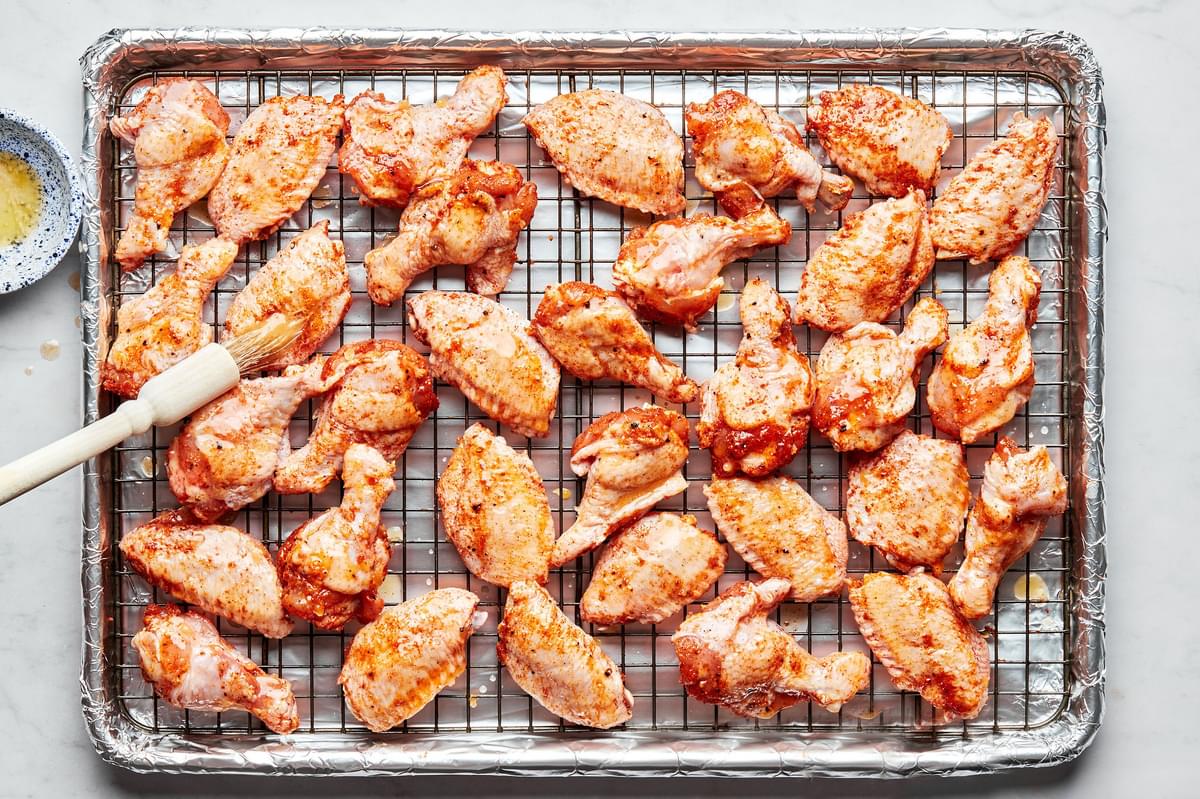 seasoned chicken wings being brushed with melted butter on a cooling rack on top of a foil lined baking sheet.