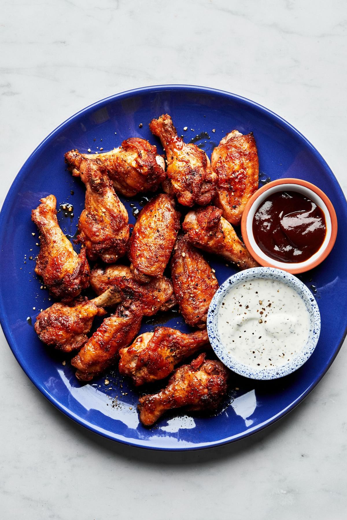 Homemade baked chicken wings on a plate served with ranch dressing and bbq sauce in small bowls