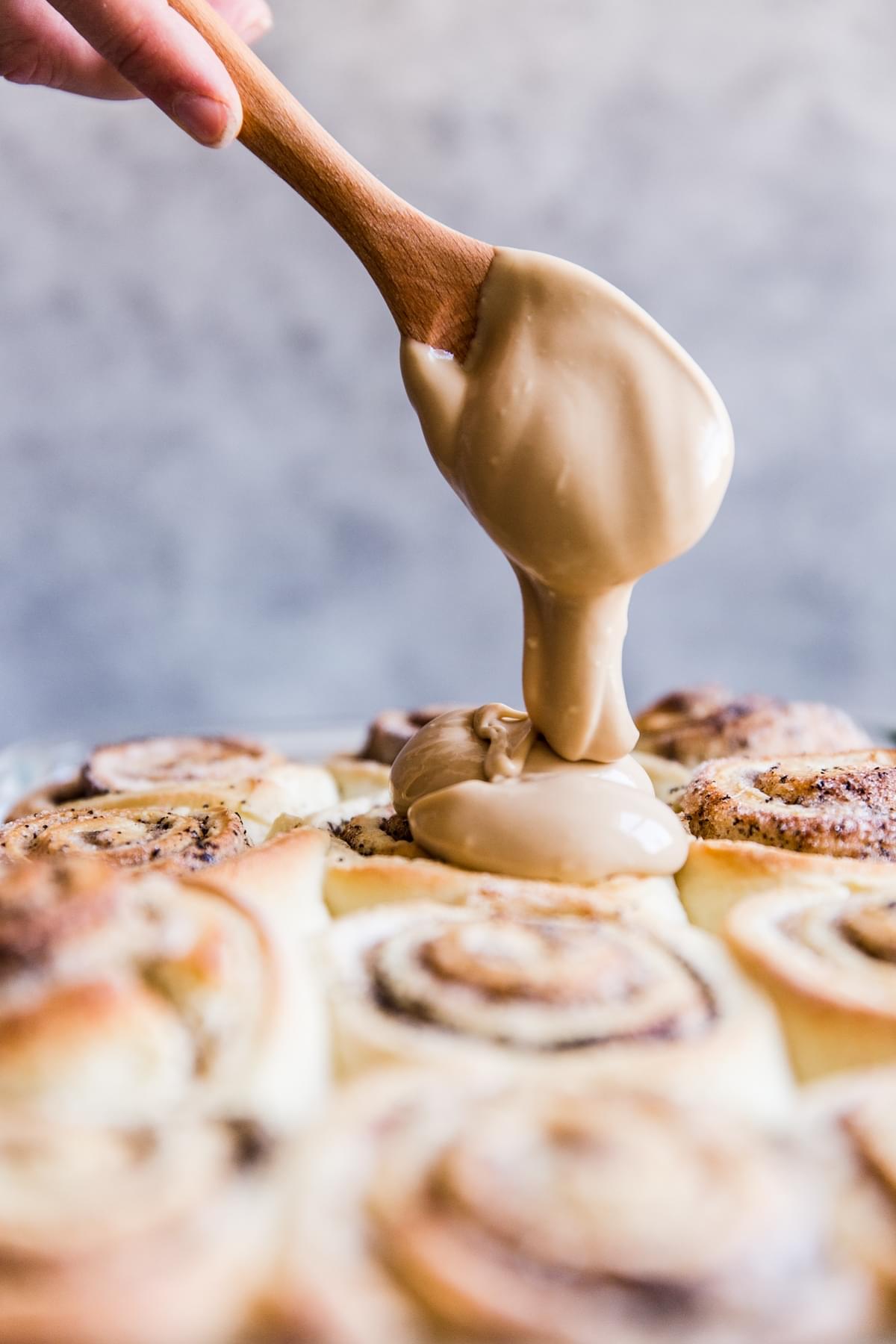 maple cream cheese frosting being dolloped onto coffee cinnamon rolls