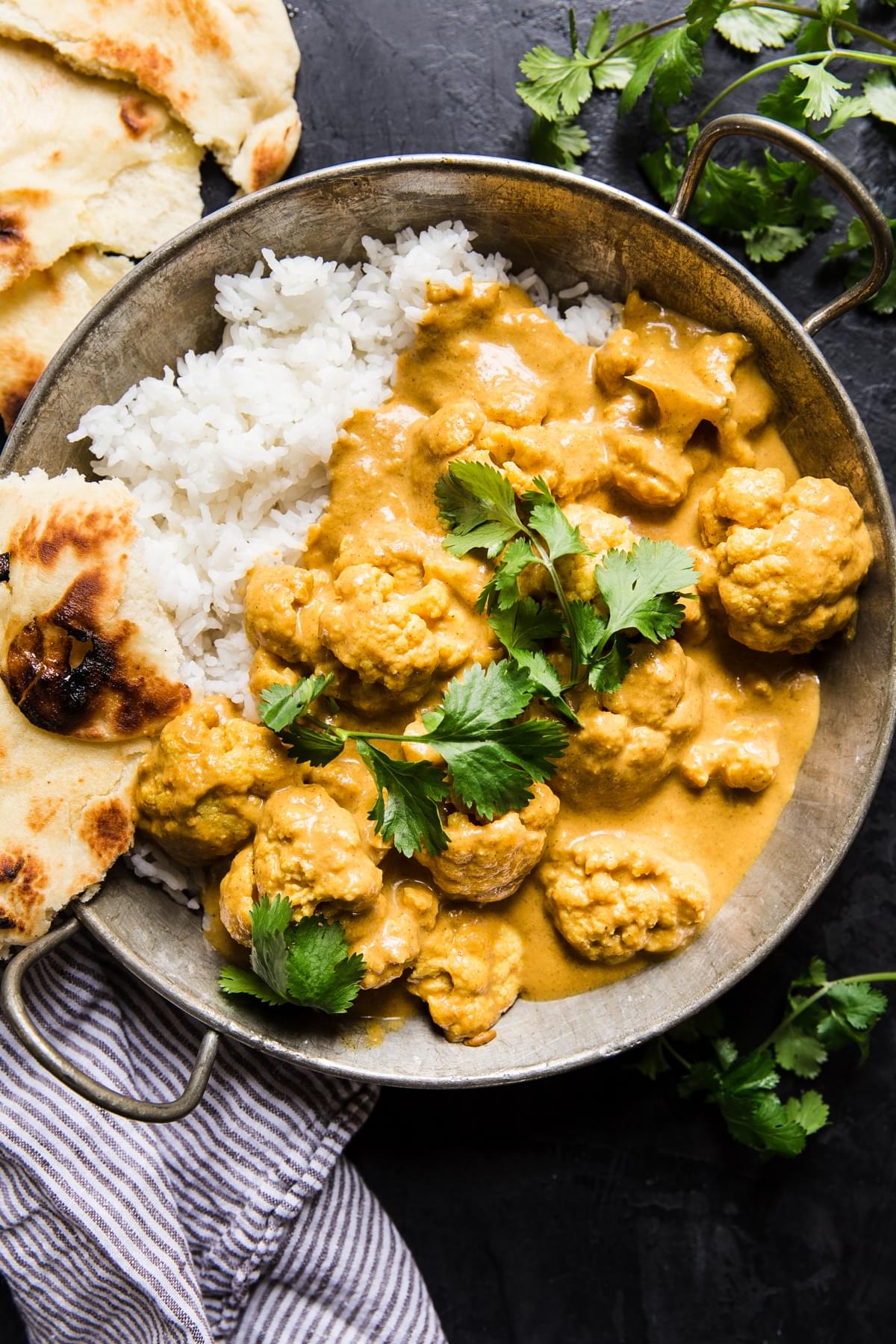 creamy vegan cauliflower curry with white rice and torn naan in a serving bowl