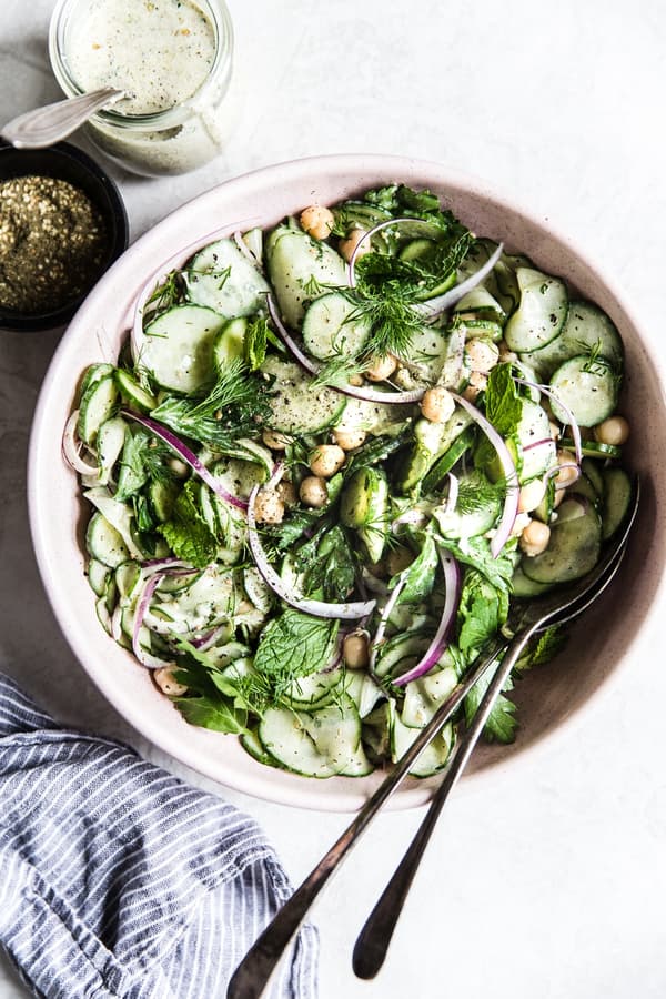 Thin-sliced cucumber dressed up with onions, mint, and garbanzo beans in a light-pink bowl.
