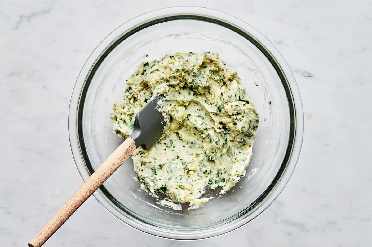 butter, parsley, garlic, garlic powder, salt and parmesan being stirred in a bowl to make a spread for french bread pizza