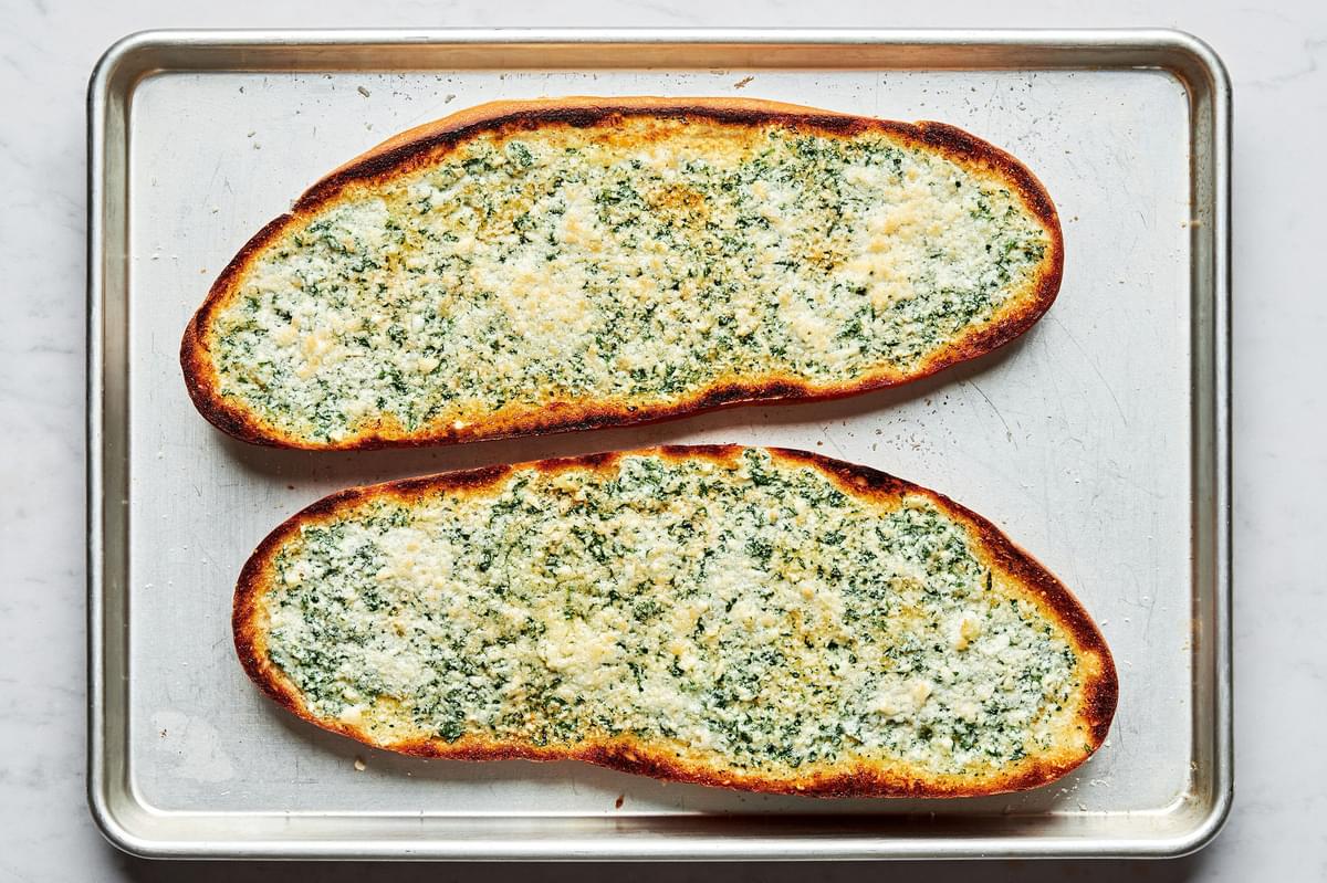 a loaf of french bread sliced in half topped with a butter parmesan spread on a baking sheet to make french bread pizza