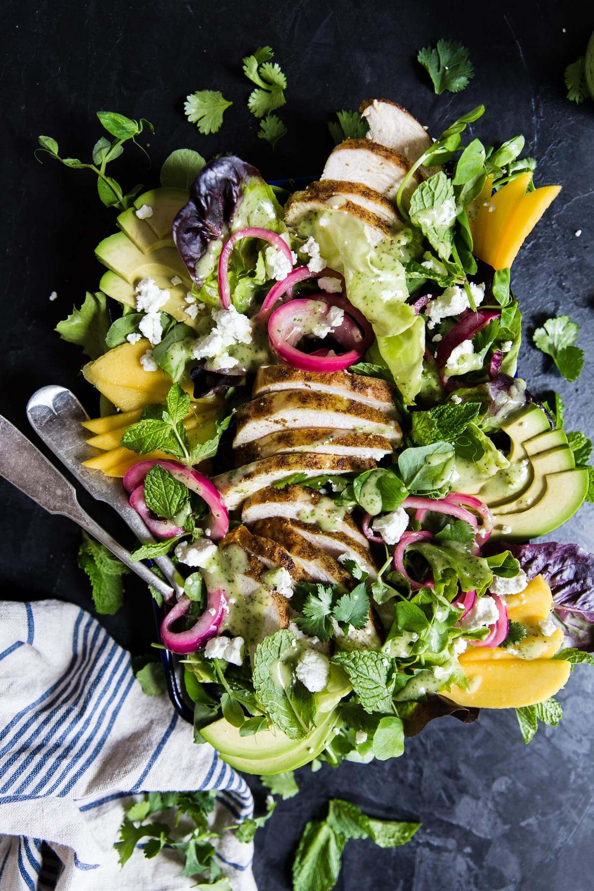 Grilled curry chicken salad with herb vinaigrette, mango, goat cheese, pickled onions, mint and cilantro on a serving plate