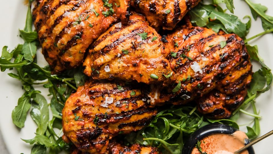 Grilled harissa chicken on a plate with arugula