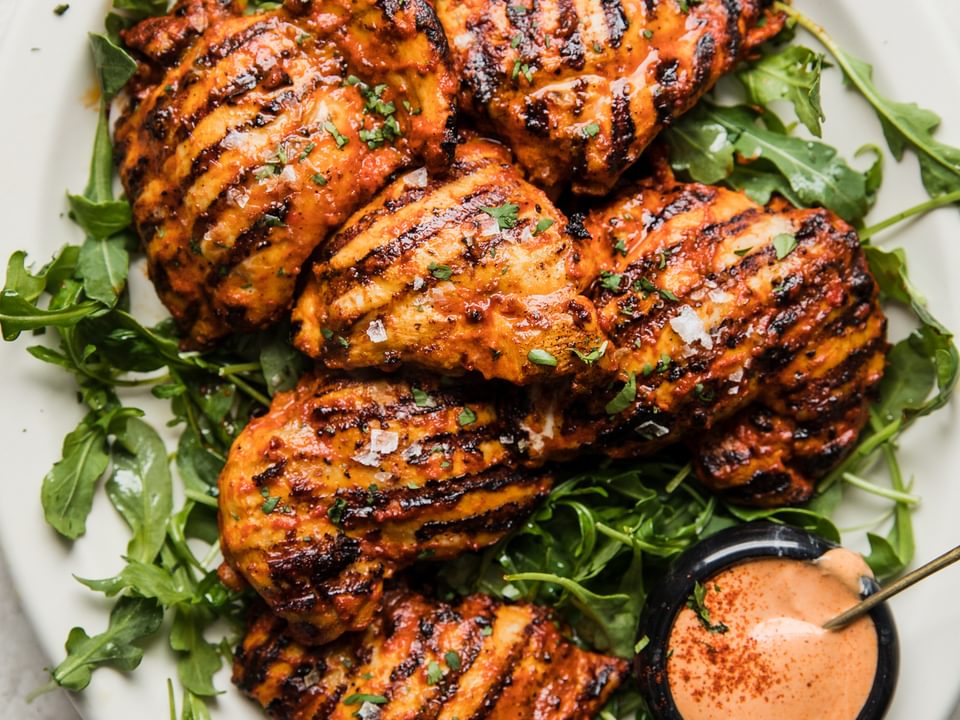 Grilled harissa chicken on a plate with arugula