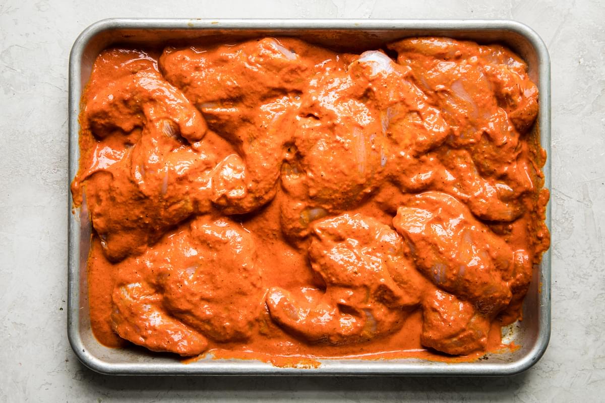 boneless skinless chicken thighs on a rimmed baking sheet covered in harissa marinade