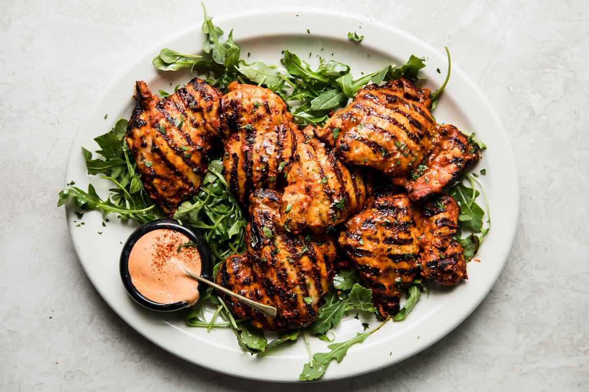 a plate of arugula topped with harissa chicken with harissa mayonnaise