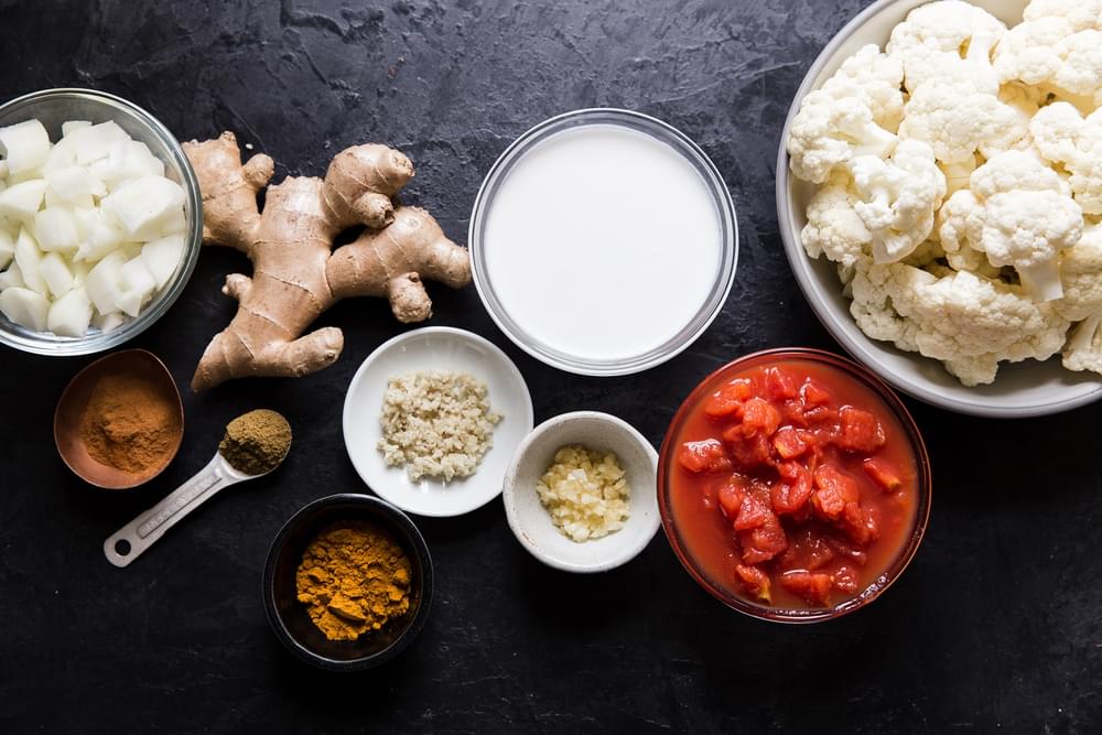 Ingredients laid out for vegetarian cauliflower curry; cauliflower, coconut milk, ginger, garlic, turmeric, tomatoes