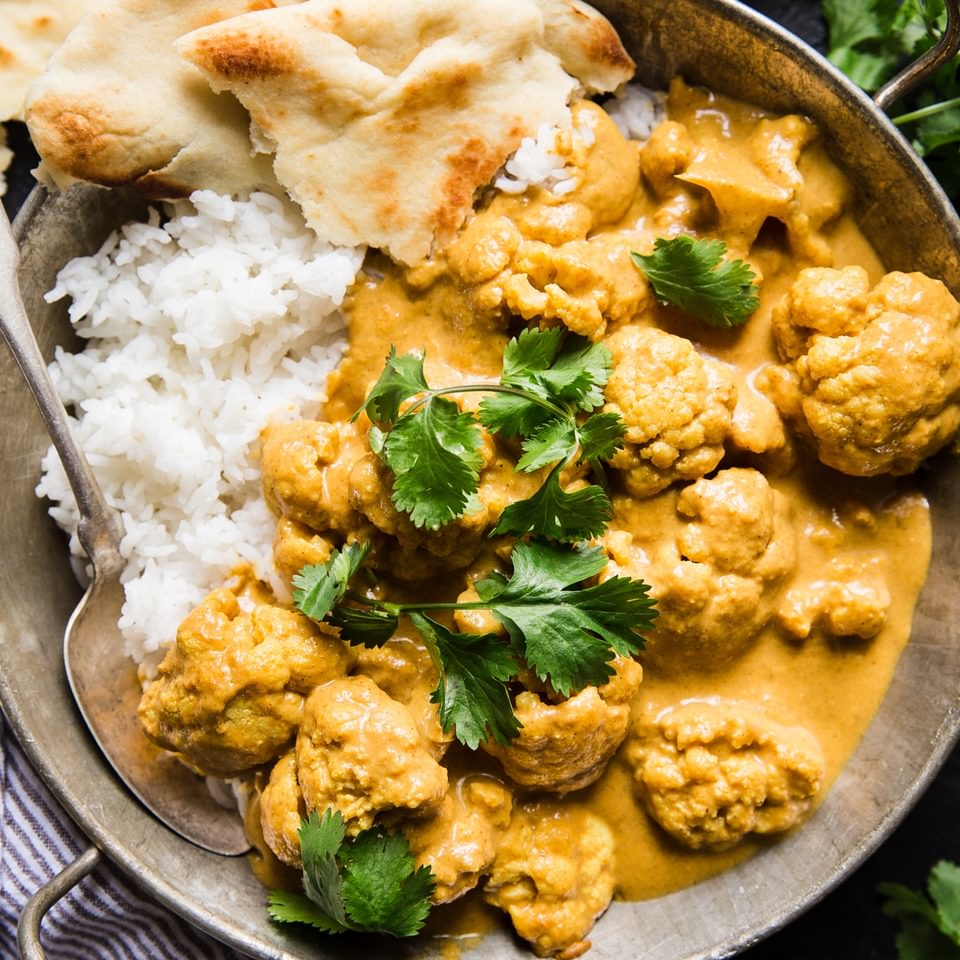 creamy Indian cauliflower curry with rice and torn naan in a large serving bowl