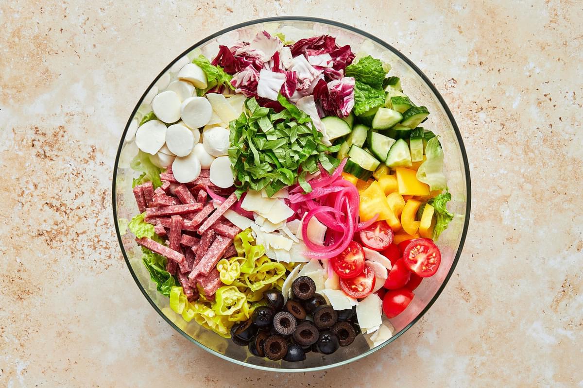 ingredients for homemade Italian chopped salad in a bowl together including lettuce, salami, pickled onions and mozzarella