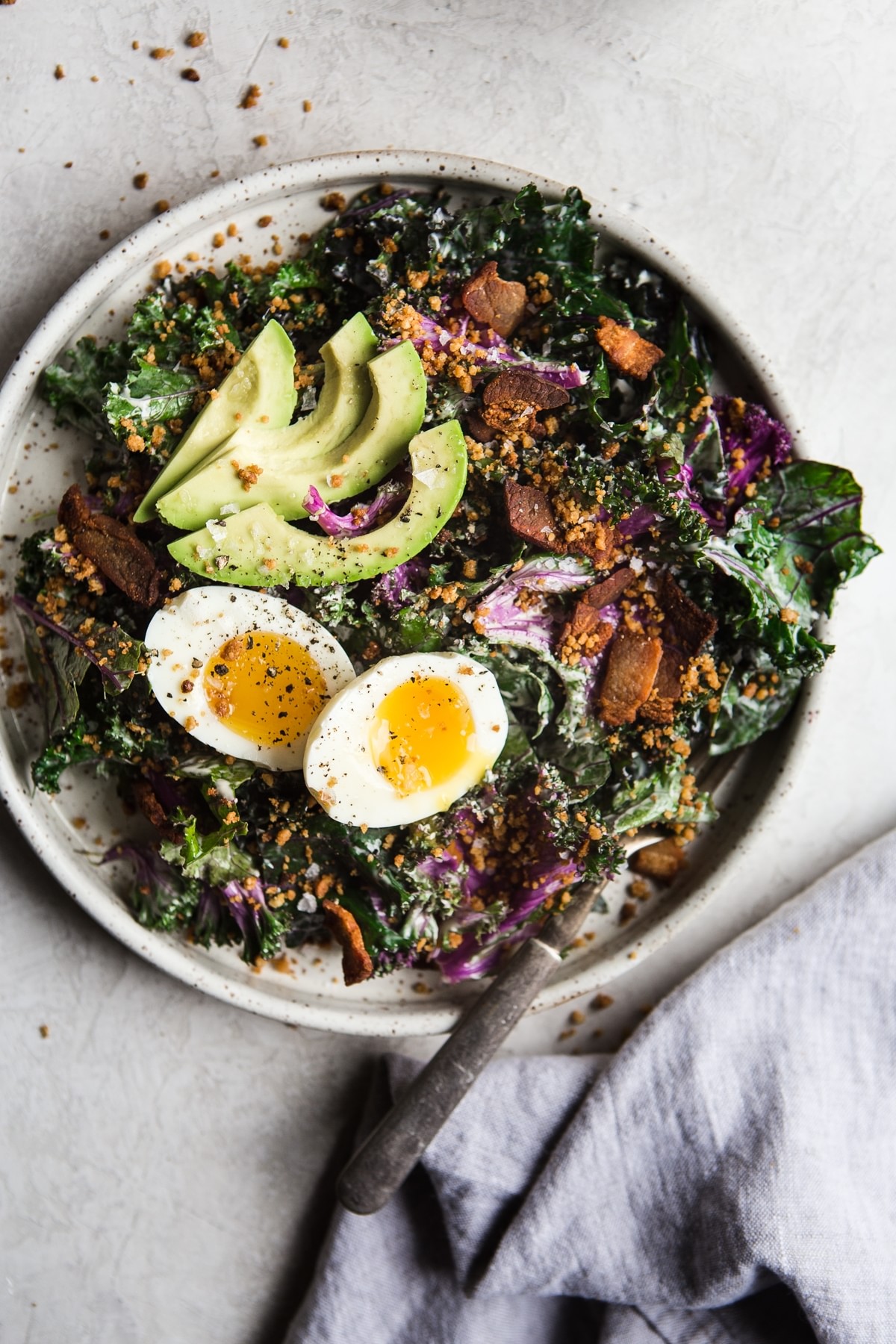 whole 30 kale caesar salad with avocado, bacon and soft boiled egg on a plate