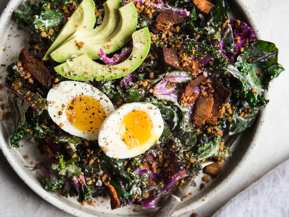 whole 30 kale caesar salad with avocado, bacon and soft boiled egg on a plate