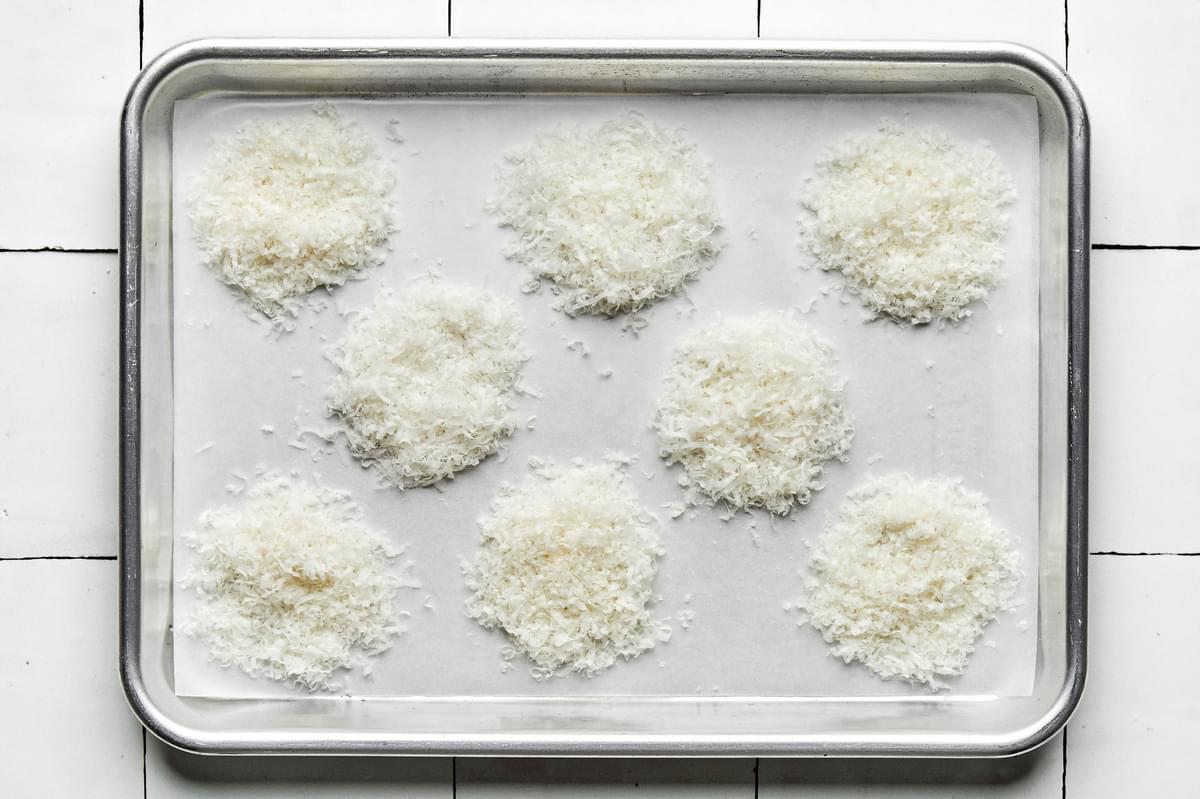 tablespoon sized piles of grated parmesan cheese on a parchment lined baking sheet