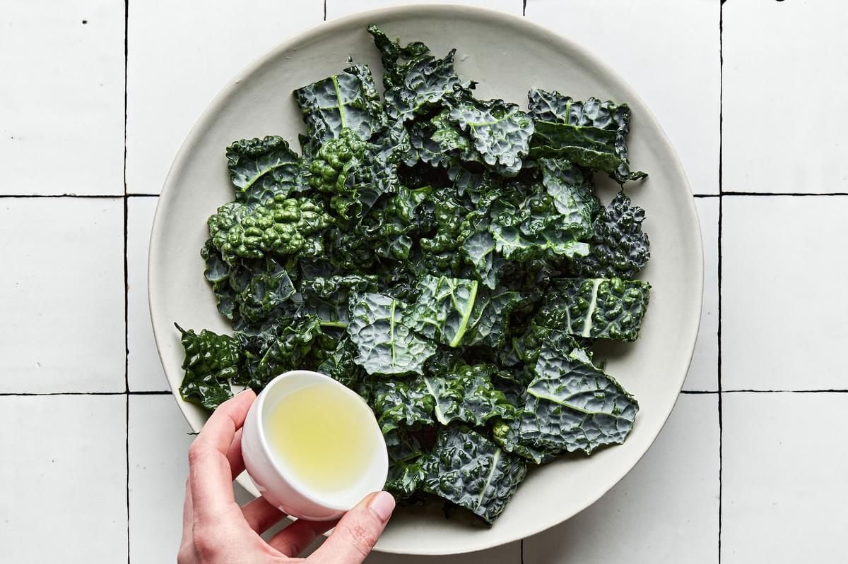 lemon juice being poured on top of chopped kale in a bowl