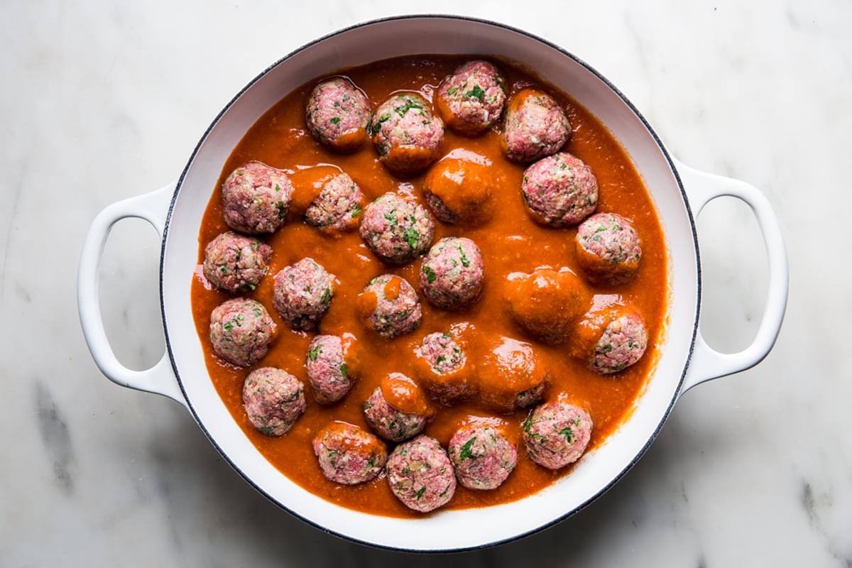 raw Italian meatballs in a braiser with marinara sauce