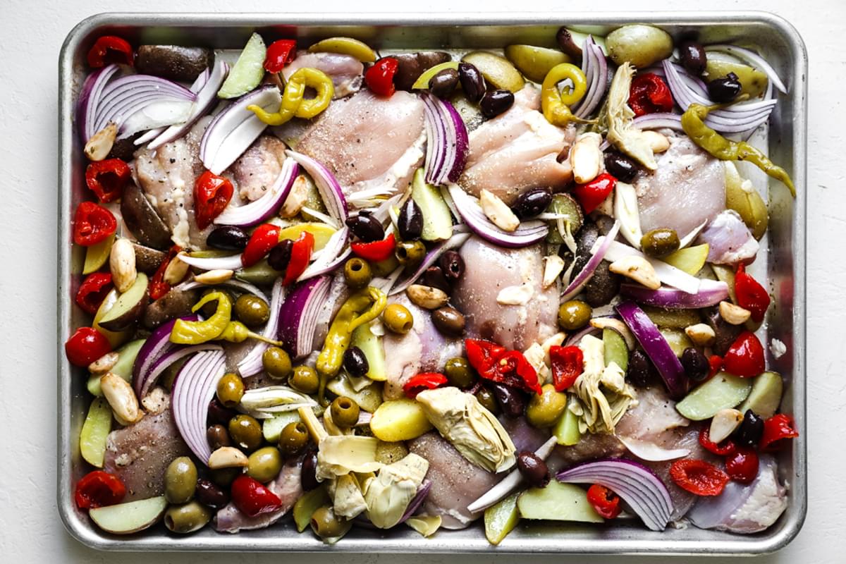 par cooked potatoes on a baking sheet with chicken thighs, olives, red onions and peppers from olive bar