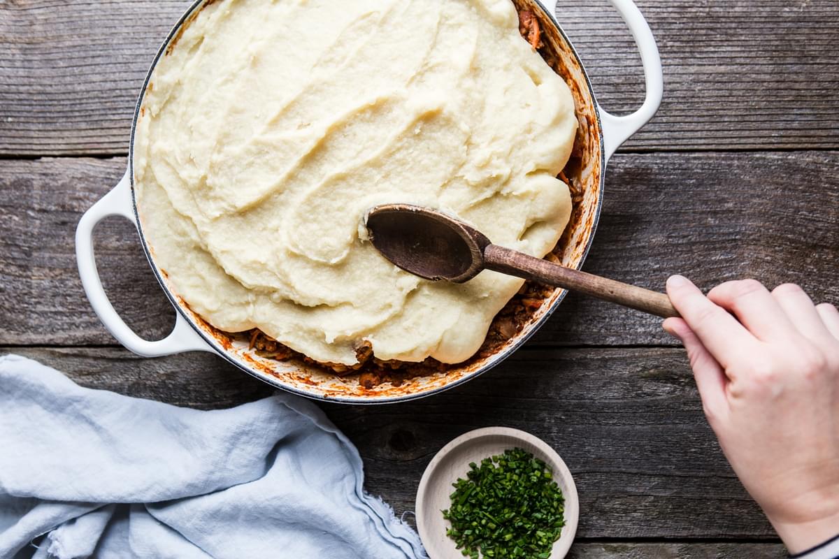 hand spreading parsnip puree on the top of a shepherd's pie