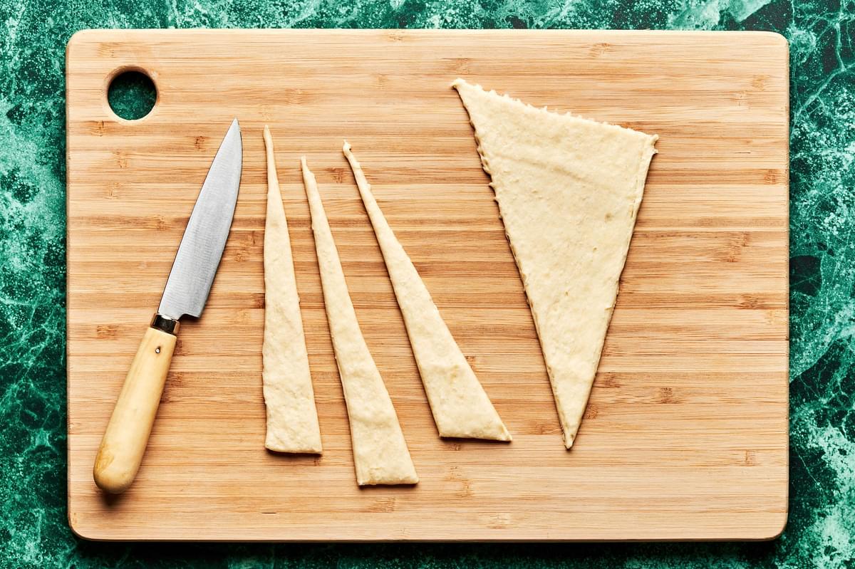 crescent rolls being sliced into triangles on a cutting board