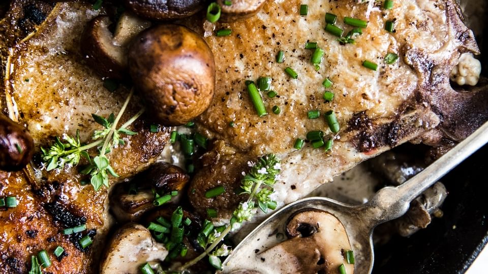Pork Chops With Mushroom Cream Sauce in a pan with thyme and a spoon