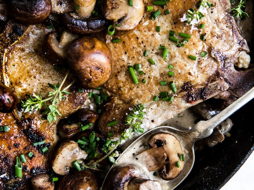 Pork Chops With Mushroom Cream Sauce in a pan with thyme and a spoon