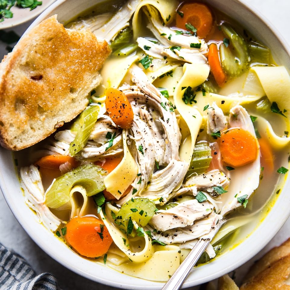 a bowl of quick and easy chicken noodle soup with a piece of bread and a spoon.