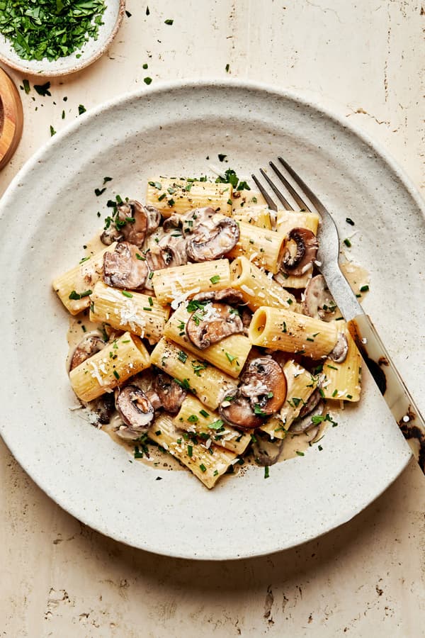 homemade rigatoni with mushroom sauce in a pasta bowl with a fork made with cream, parmesan, chives, parsley and wine