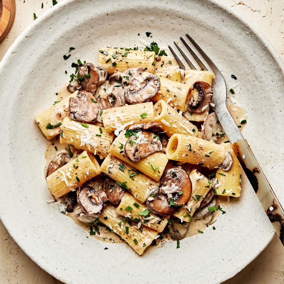 homemade rigatoni with mushroom sauce in a pasta bowl with a fork made with cream, parmesan, chives, parsley and wine