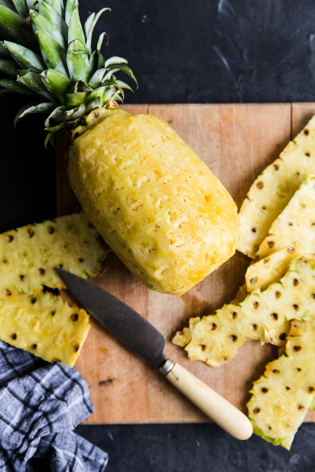 a whole pineapple peeled on a cutting board with a knife