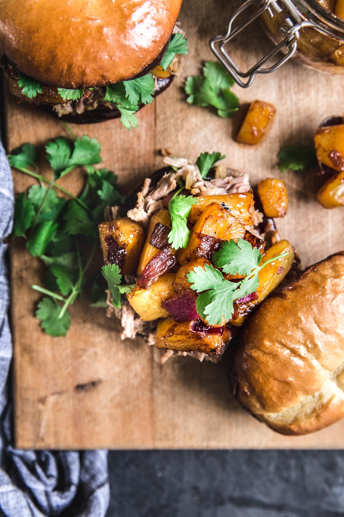 pulled pork sandwiches with cilantro, pineapples and caramelized red onions on a cutting board.