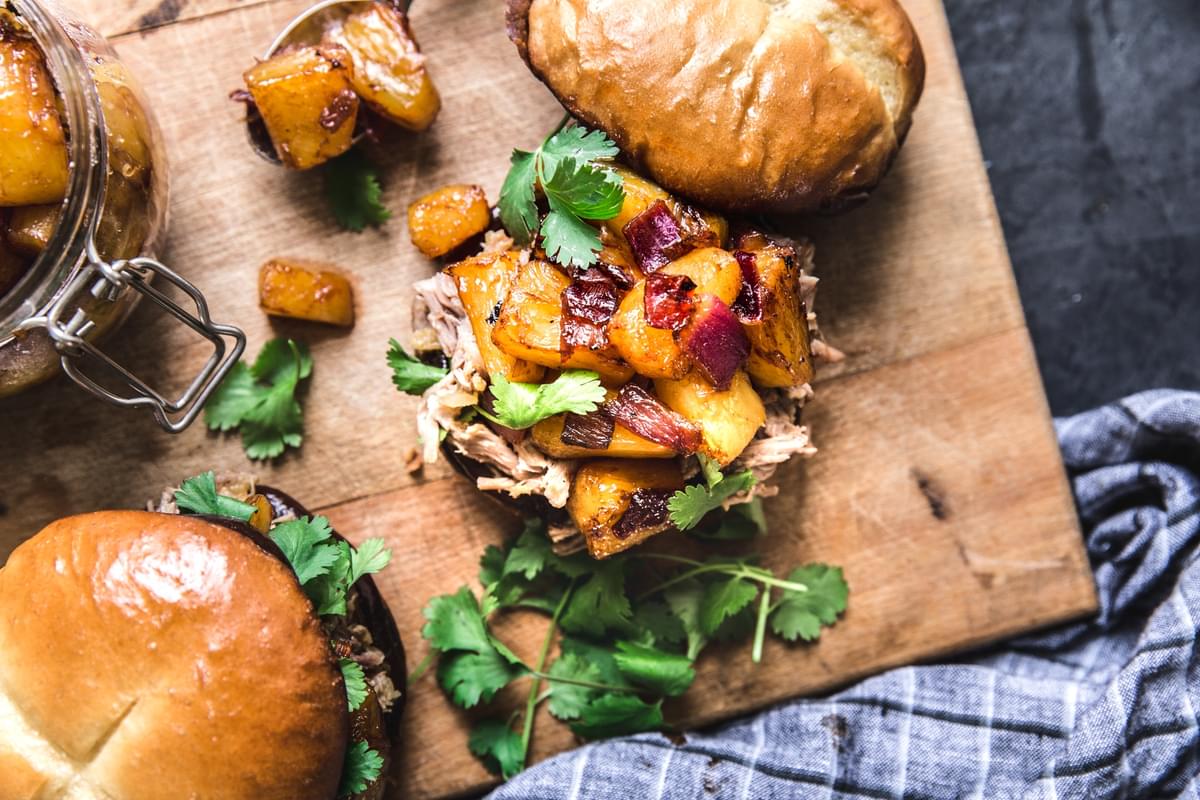 pulled pork sandwiches with cilantro, pineapples and caramelized red onions on a cutting board.