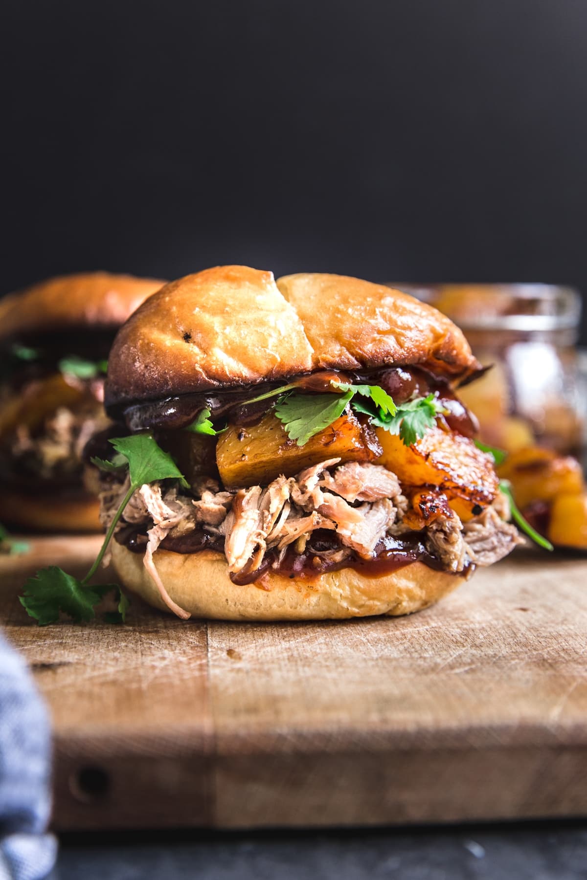 slow cooker pork sandwich with cilantro pineapples, onions and bbq sauce on a bun on a butting board.