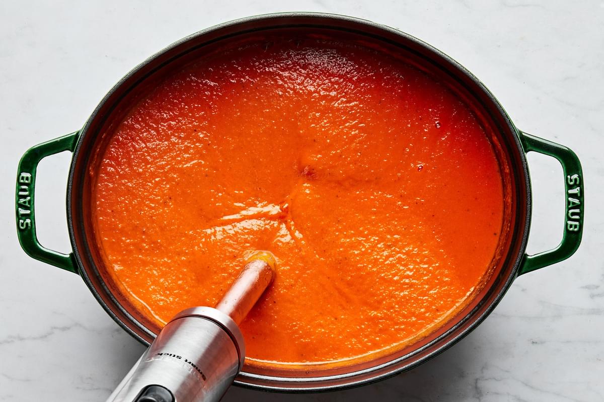 homemade tomato bisque being blended with an immersion blender in a soup pot
